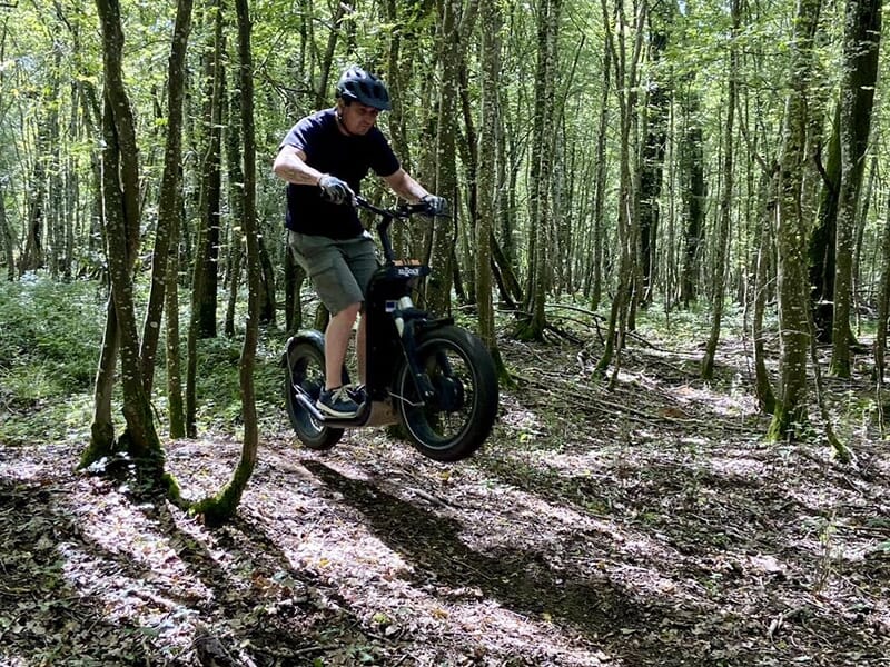 Un randonneur effectue un saut lors d'une balade sportive en forêt en trottinette électrique.