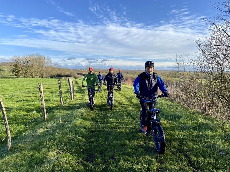 Des randonneurs en trottinettes électriques sillonnent la campagne avec une forêt et un ciel bleu en toile de fond