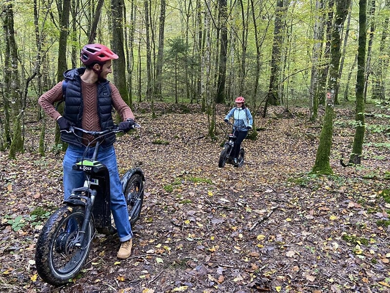 Un homme attend sa femme lors d'une randonnée en trottinette électrique dans la forêt.