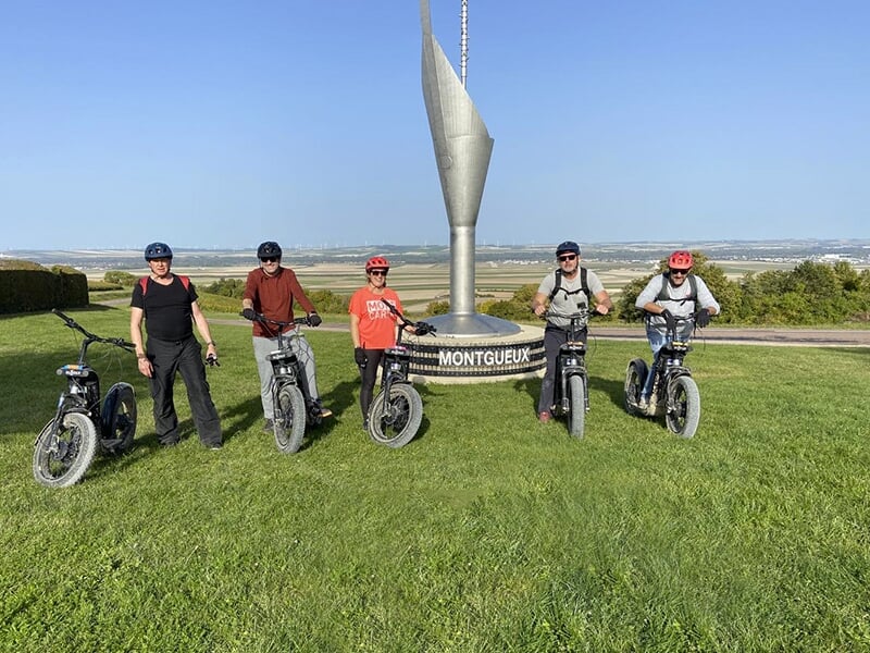 Des touristes en trottinette électrique tout-terrain posent devant un monument de la ville de Montgueux dans le département de l'Aube