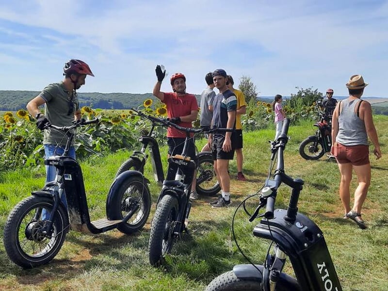 Un groupe de randonneurs en trottinette électrique tout-terrain fait une pause sur un chemin de campagne avec un champ de tournesols en arrière-plan