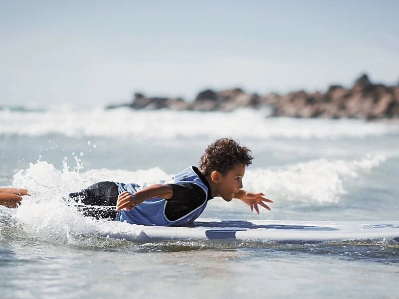 un jeune garçon nage à plat ventre sur sa planche