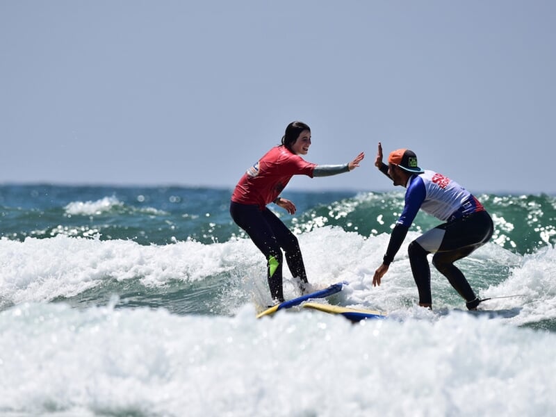 Deux surfeurs en combinaison rouge et bleue s'encouragent en se tapant dans la main sur une planche dans l'eau.