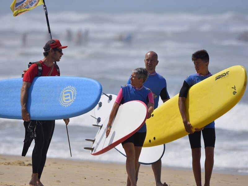 Trois surfeurs marchent sur la plage avec leurs planches, discutant avant de rejoindre l'eau à Seignosse.