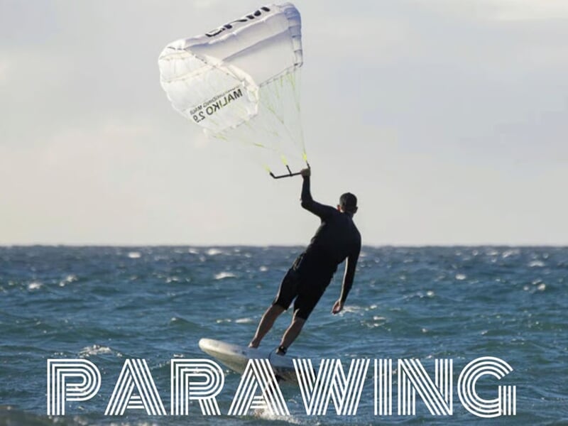 Personne pratiquant le parawing sur l'eau, tenant une voile blanche avec l'inscription ONJAM, ciel clair en arrière-plan.