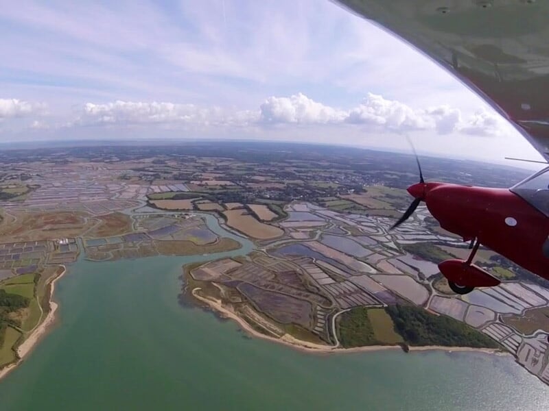 Vue aérienne prise depuis un petit avion rouge survolant les méandres de la Loire et des terres agricoles sous un ciel partiellement nuageux.