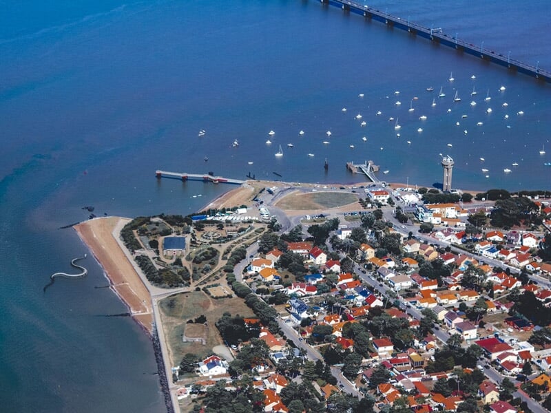 Vue aérienne de Saint-Nazaire avec son port, des voiliers sur l'eau et un pont au loin sous un ciel clair.