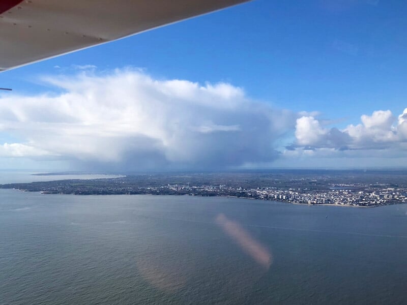 Vue aérienne de la côte de Saint-Nazaire avec la mer, la ville et un ciel partiellement nuageux depuis un avion ULM.