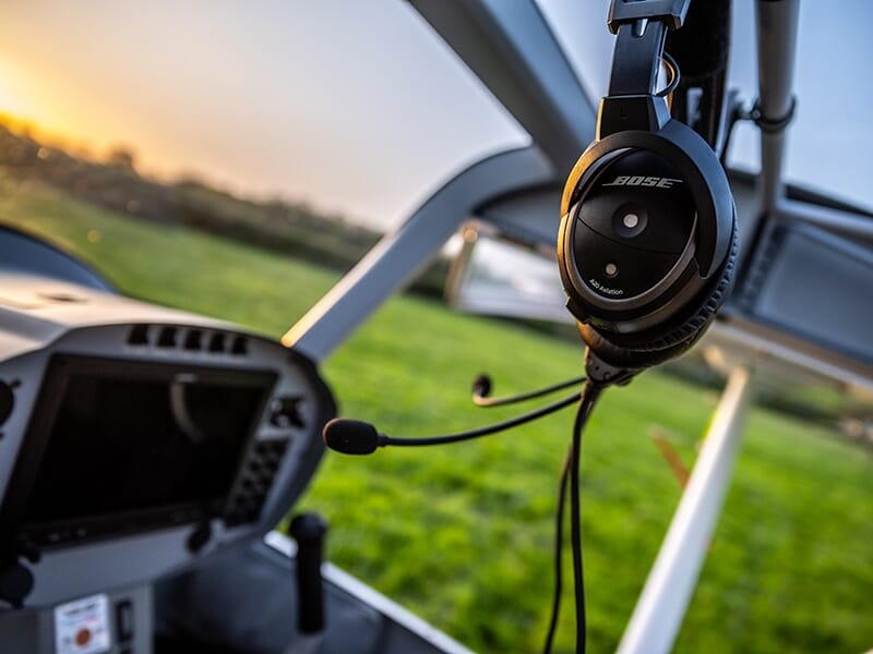 Casque d’aviation Bose suspendu dans le cockpit d’un avion léger, avec vue sur un champ en arrière-plan.
