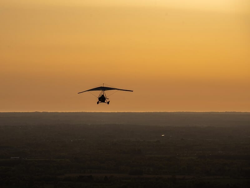 ULM pendulaire survolant une campagne au crépuscule avec vue panoramique.