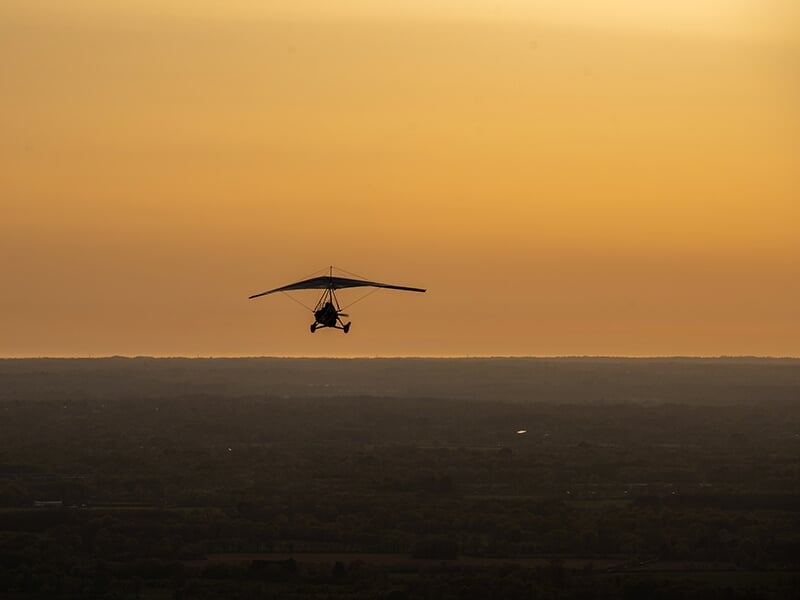 ULM pendulaire survolant une campagne au crépuscule avec vue panoramique.
