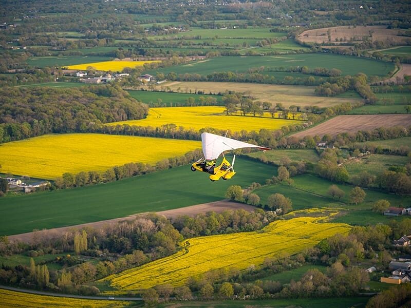 ULM pendulaire survolant des champs cultivés aux couleurs vives et contrastées.