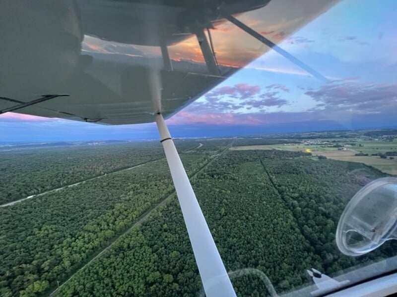 Vue aérienne depuis un petit avion au-dessus d'une vaste forêt et campagne sous un ciel coloré au coucher du soleil.