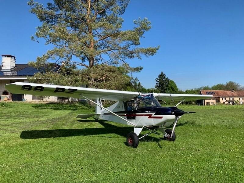 Petit avion ULM Tétras blanc avec des détails rouges et noirs posé sur une pelouse verte sous un ciel bleu clair à Mulhouse Habsheim.