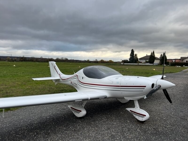 Avion ULM Dynamic avec des bandes rouges garé sur une piste d'aérodrome sous un ciel nuageux à Mulhouse Habsheim.