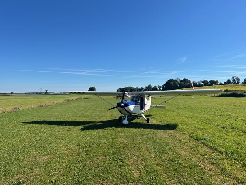 Petit avion ULM stationné sur une piste d'herbe verte sous un ciel bleu clair à l'aérodrome de Mulhouse Habsheim.