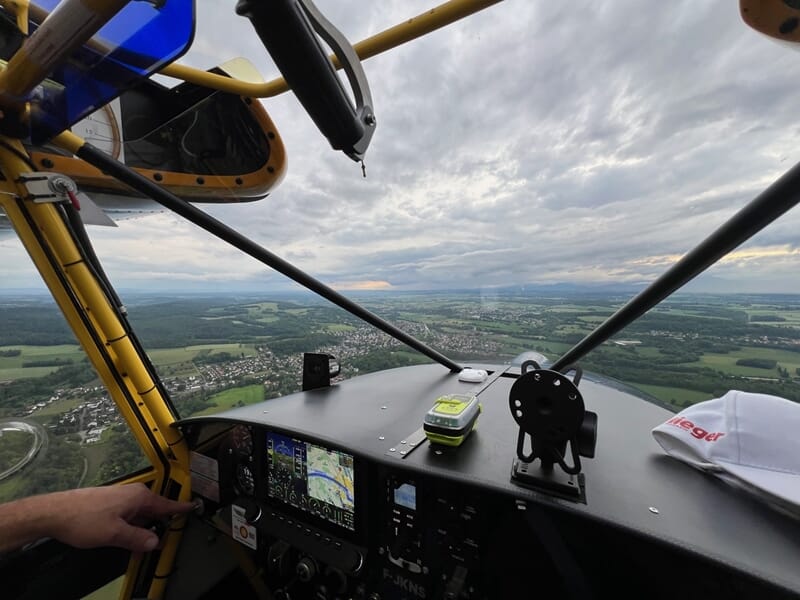 Vue depuis le cockpit d'un avion ULM avec tableau de bord et paysage de campagne sous un ciel nuageux.