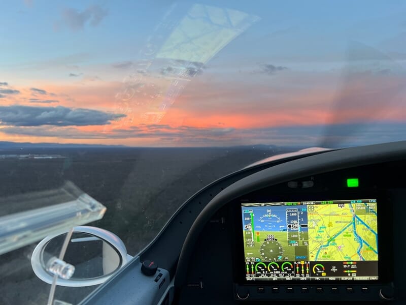 Tableau de bord d'un avion ULM au coucher du soleil avec ciel coloré et paysage sombre à l'horizon.