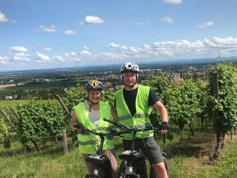 Deux personnes en trotinette électrique posent devant des vignes.