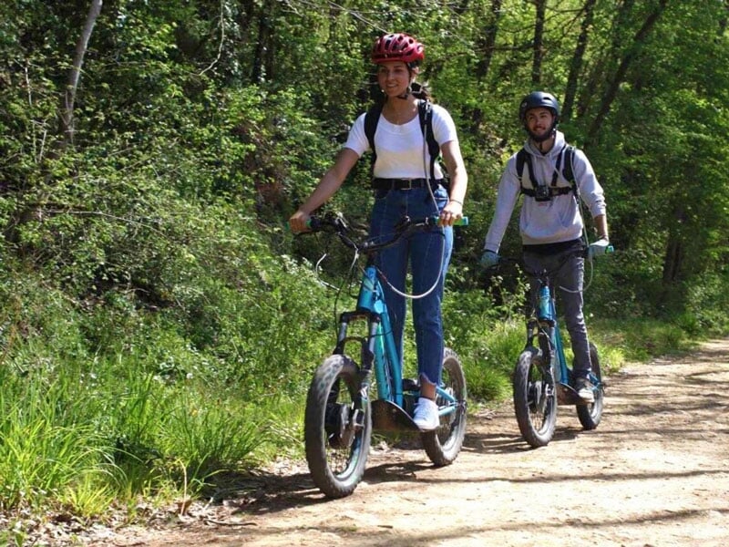 deux randonneurs se baladent dans les sous-bois en trottinette