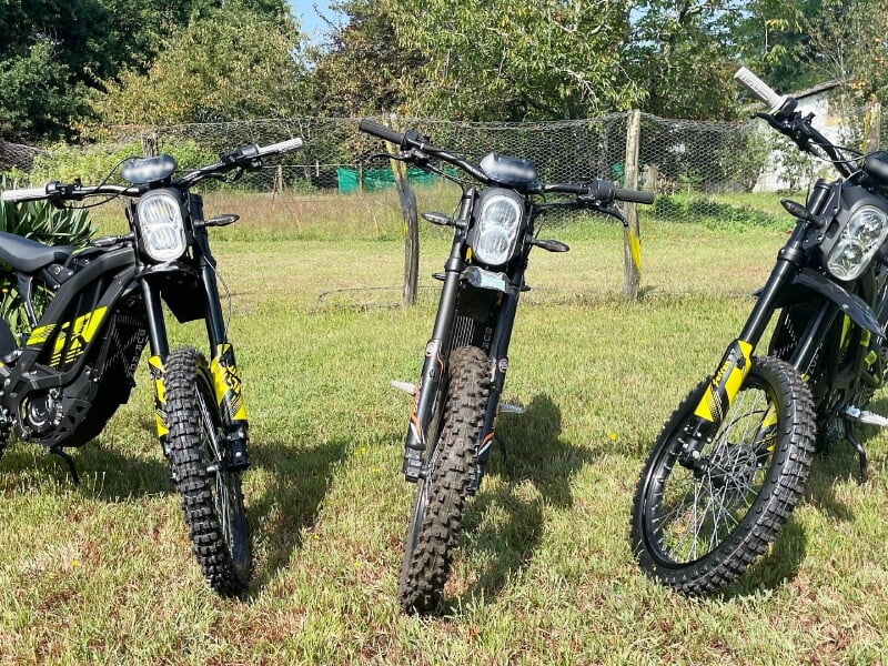 Trois trottinettes électriques tout-terrain noires avec pneus crantés, stationnées sur une pelouse verte en plein air.