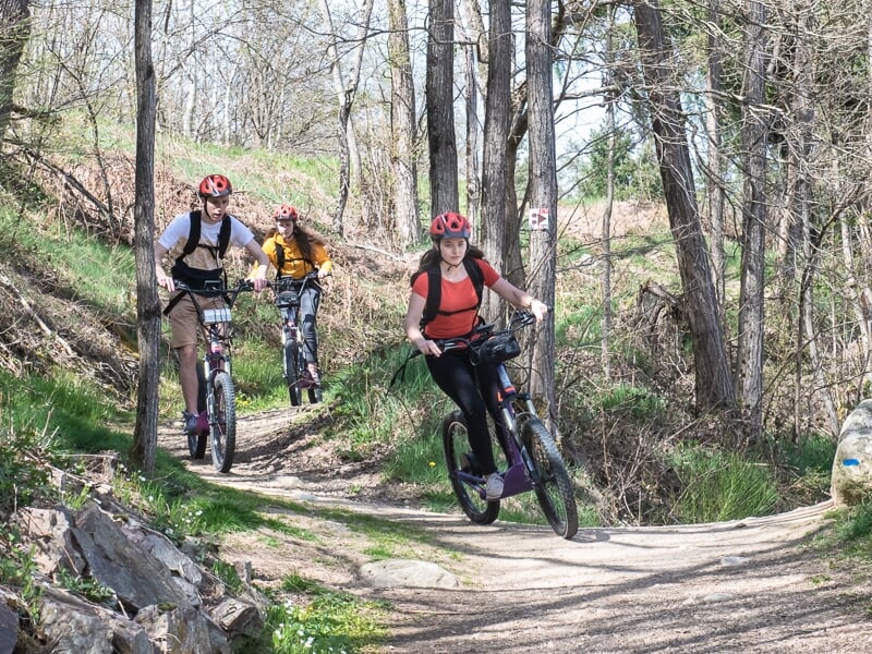 trois personnes en trottinette électrique sur un chemin de forêt