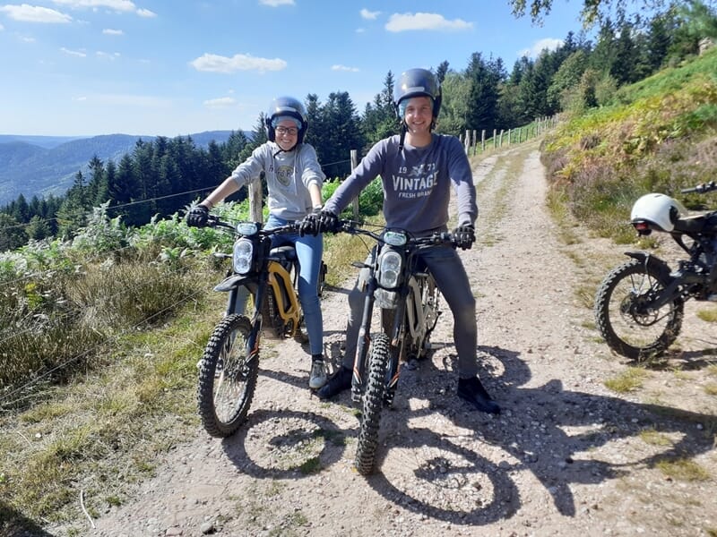Deux personnes à moto électrique sur chemin de campagne avec vue sur les Vosges.