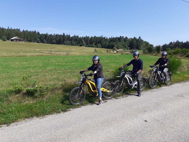 Groupe de trois personnes à moto électrique sur un chemin de campagne.