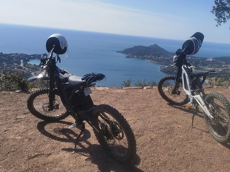 Deux vélos tout-terrain électriques avec des casques posés sur les guidons, stationnés à un point de vue élevé surplombant un paysage côtier magnifique.