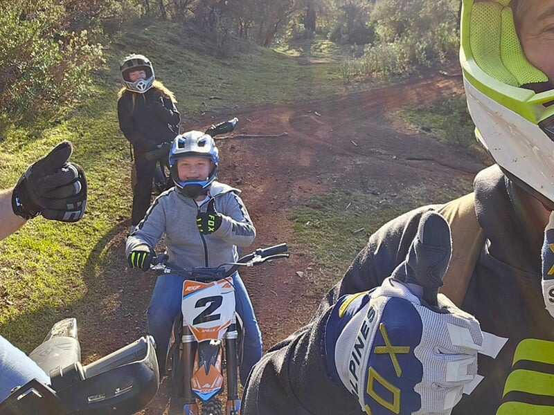 Un groupe d'amis sur des vélos tout-terrain électriques levant les pouces, montrant leur plaisir de rouler sur un sentier forestier.