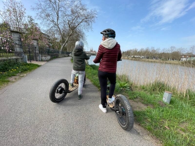 Une adulte et un enfant en trottinette électrique au bord d'un plan d'eau