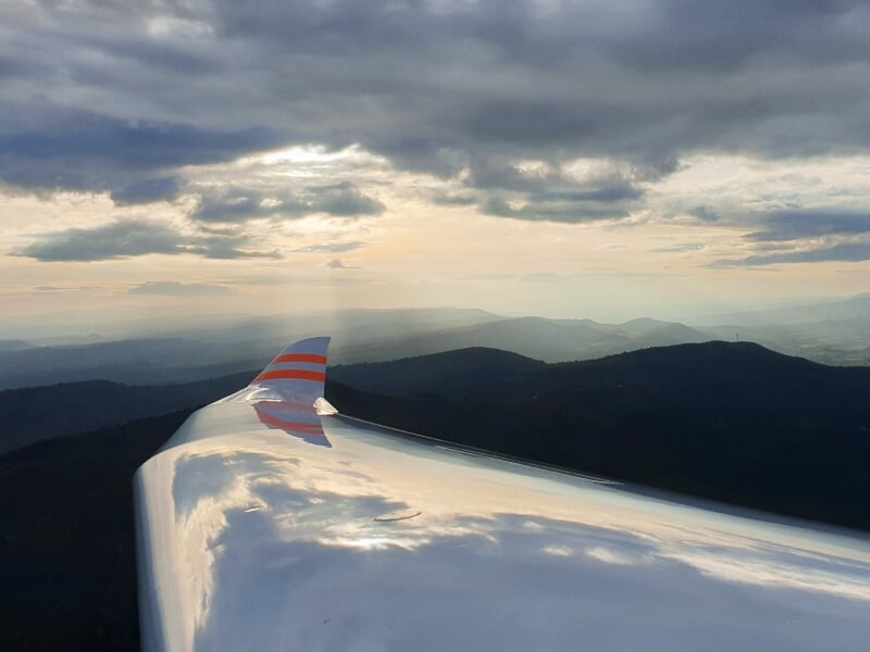 Vue depuis l'aile d'un planeur en vol au-dessus des montagnes sous un ciel nuageux à l'aérodrome de Château-Arnoux.