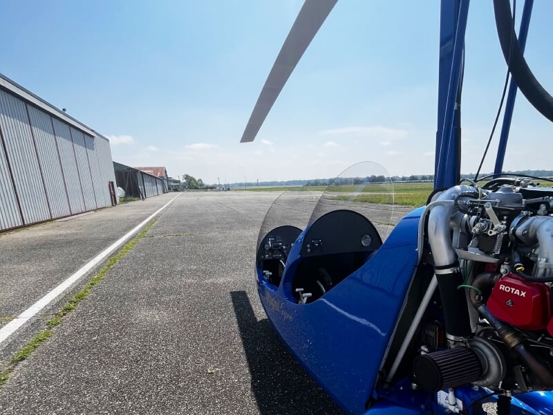 Vue rapprochée d'un ULM bleu stationné sur une piste d'aérodrome sous un ciel clair et ensoleillé.