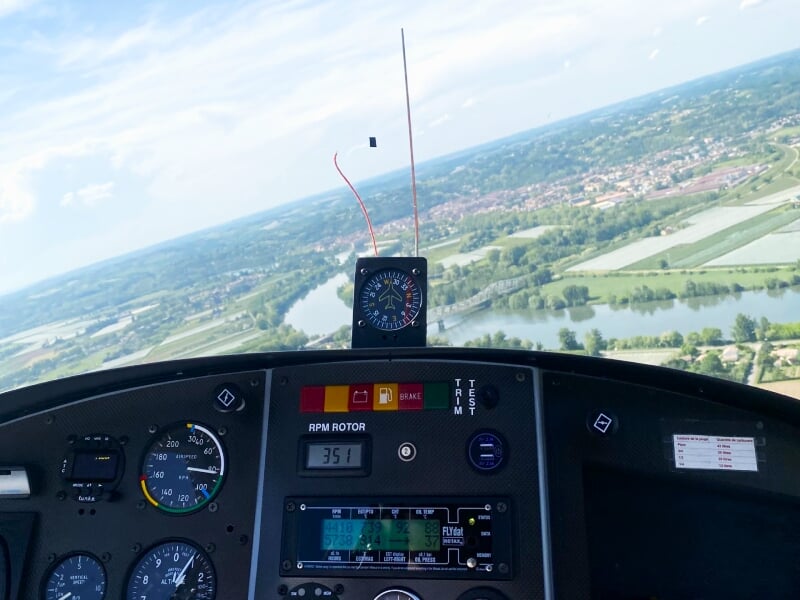 Vue depuis le cockpit d'un ULM en vol au-dessus de la campagne avec instruments de bord visibles et paysage verdoyant