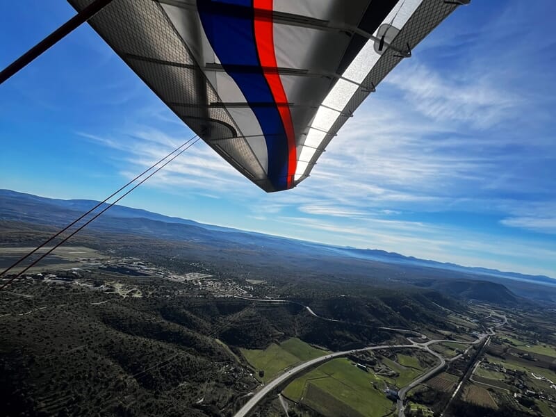 Vue aérienne prise depuis un ULM au-dessus d'un paysage vallonné avec une aile d'ULM visible au premier plan.