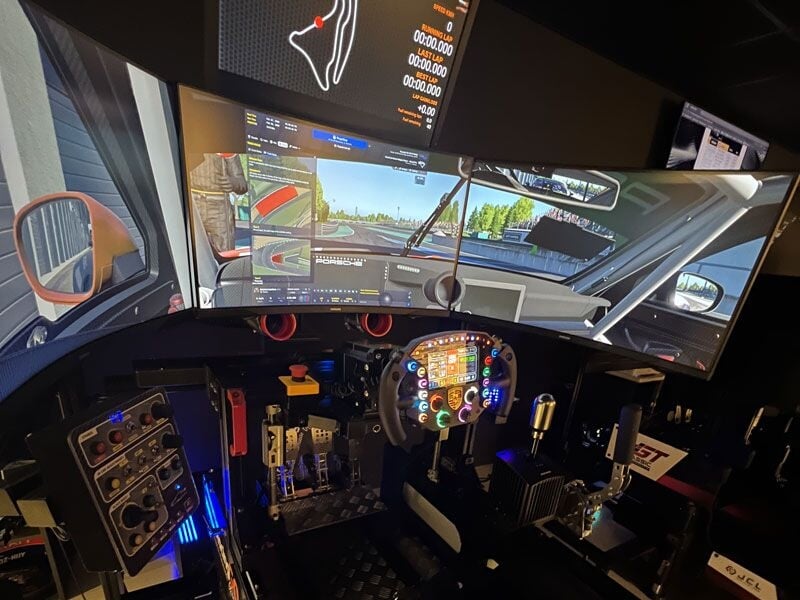 Intérieur d'un simulateur de conduite avec volant, pédales et écrans affichant une course virtuelle.