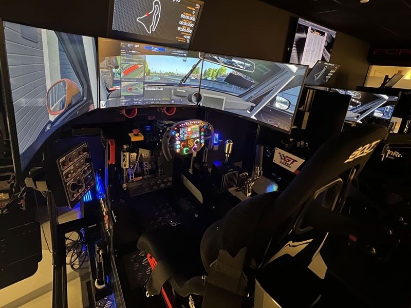 Siège et volant d'un simulateur de course automobile avec plusieurs écrans et équipements de pilotage.