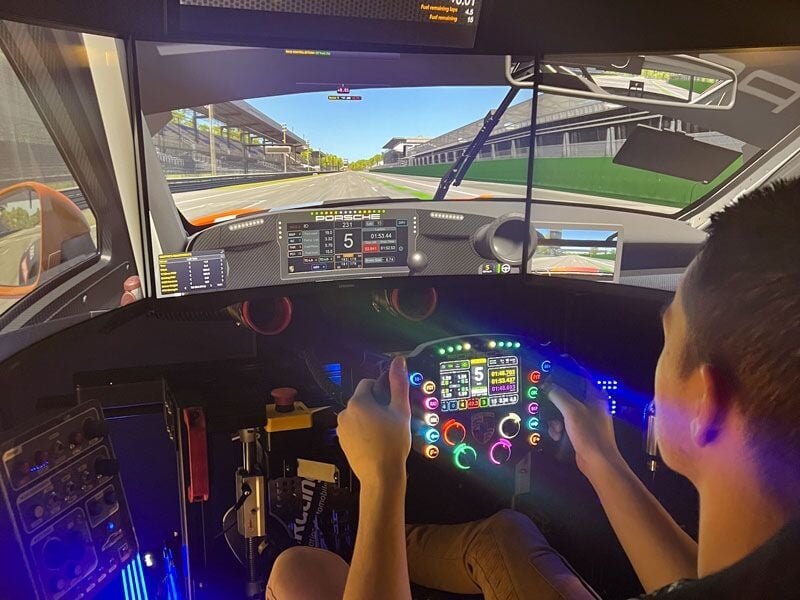 Conducteur utilisant un simulateur de course avec volant et affichage numérique sur plusieurs écrans.