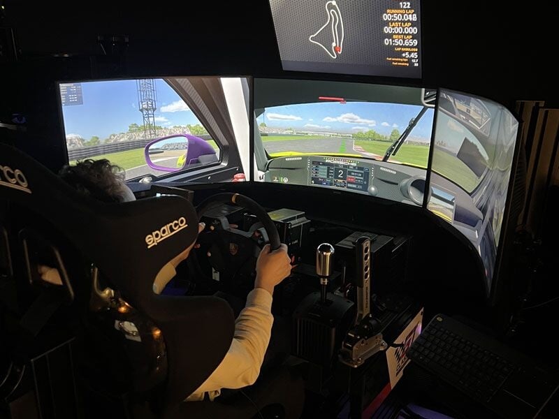 Personne au volant d'un simulateur de course automobile avec vue sur piste et tableau de bord digital.