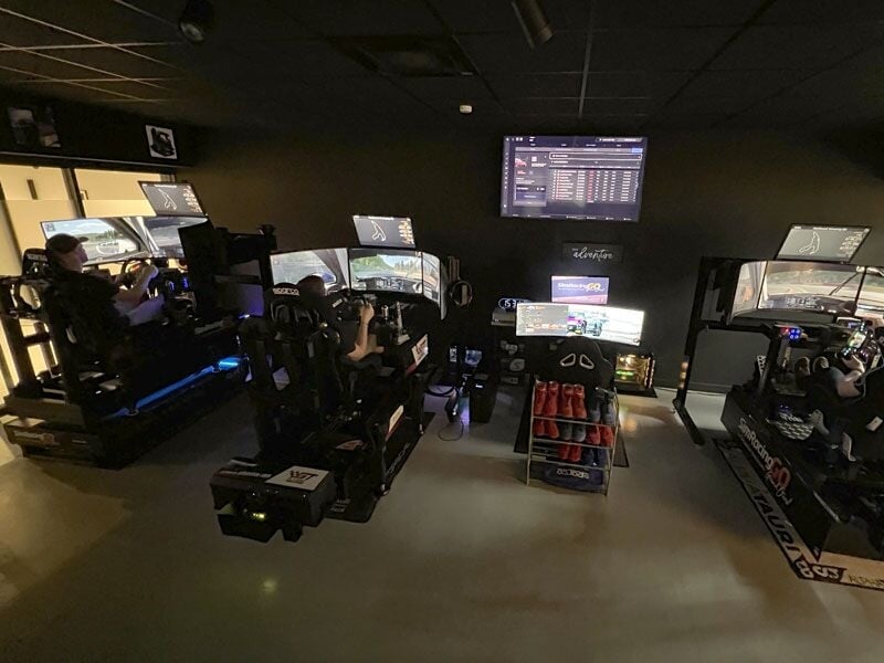 Simulateur de conduite automobile avec siège baquet, volant et plusieurs écrans dans une salle dédiée.
