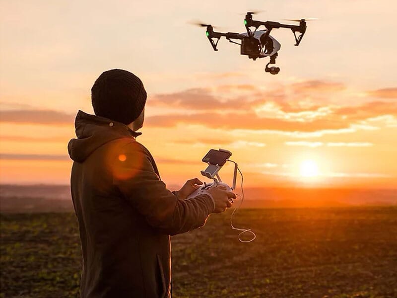 un télépilote fait voler son drone au coucher du soleil