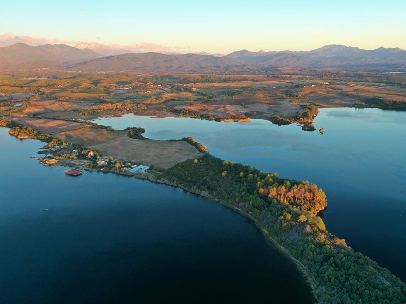 Vue aérienne d'un paysage lacustre au coucher du soleil, avec des montagnes au loin et des îlots arborés