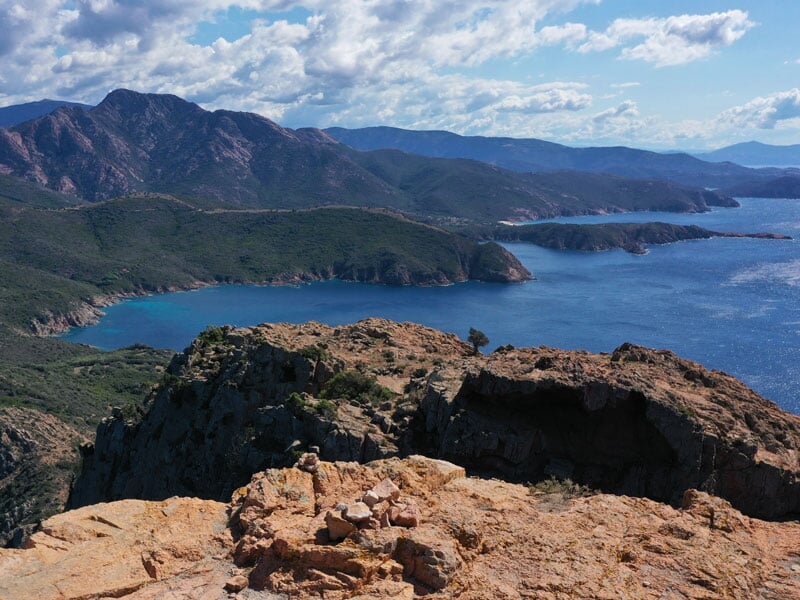 Vue panoramique sur une côte montagneuse, eaux bleues profondes et montagnes en arrière-plan sous un ciel nuageux