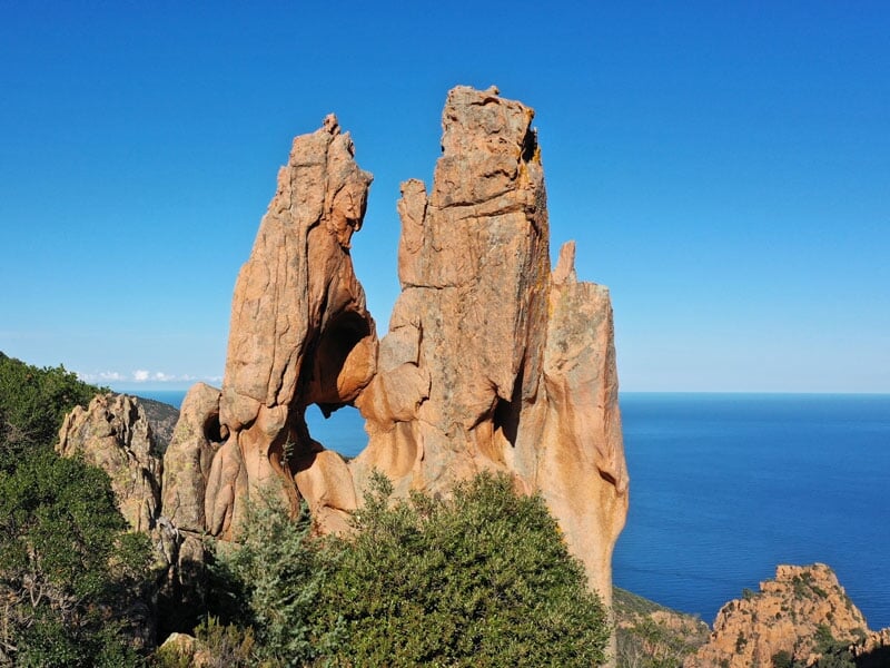 Formation rocheuse spectaculaire avec un trou naturel, surplombant la mer sous un ciel bleu clair