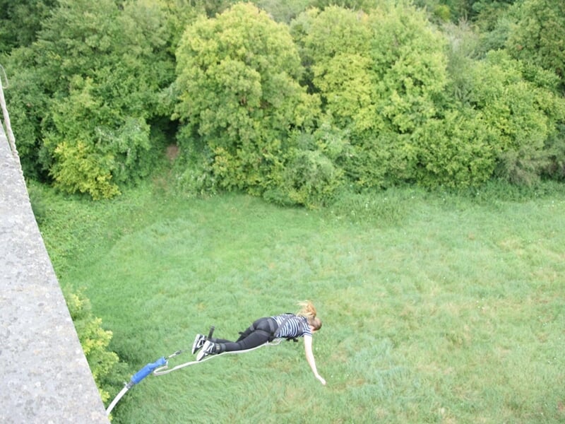 Personne en t-shirt vert clair et short sautant à l'élastique depuis un viaduc en pierre dans la nature.
