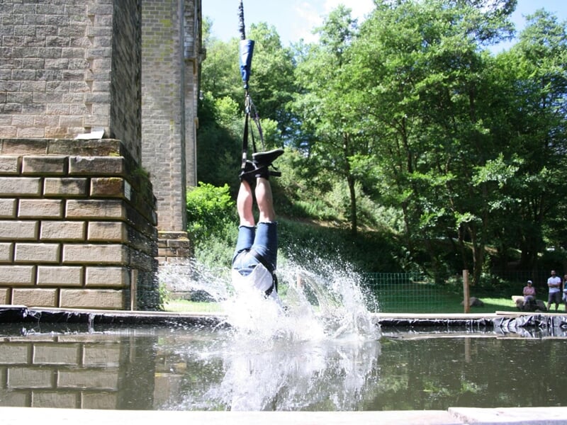 Saut à l'élastique avec une personne plongeant tête la première dans un bassin d'eau entouré d'arbres.