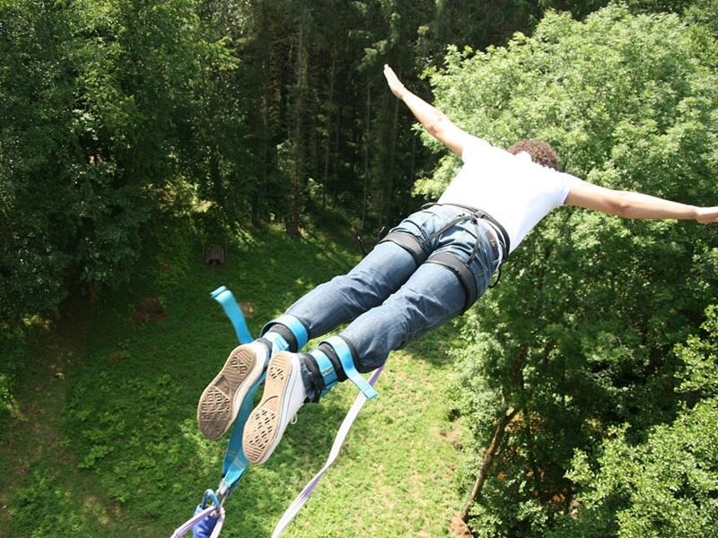 Personne en short et t-shirt bleu plongeant dans un bassin d'eau lors d'un saut à l'élastique.