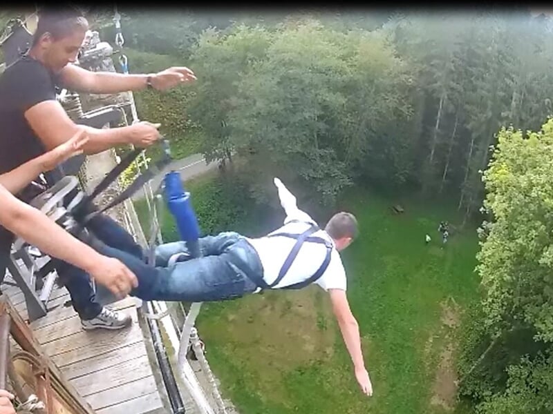 Personne suspendue à l'élastique plongeant dans un bassin d'eau entouré d'arbres et de nature.