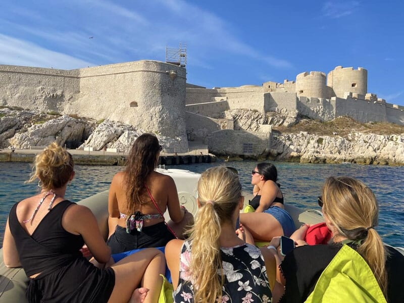 un groupe de personnes de dos à l'avant d'un bateau observe les ruines d'une forteresse en bord de mer