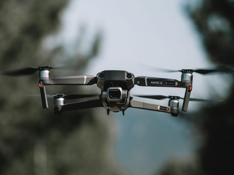 Un drone Mavic 2 en vol stationnaire avec un arrière-plan naturel flou, montrant les détails du drone en plein air.